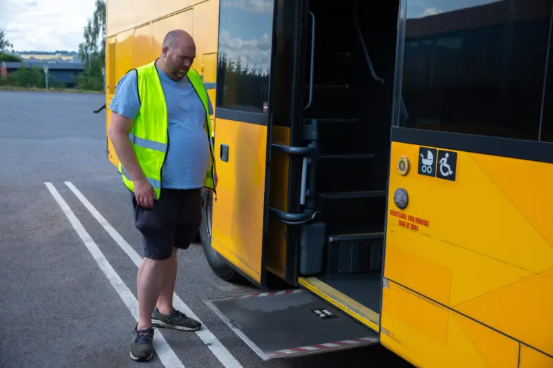 Man i gul varselväst står vid utdragen handikappramp på bussens sida.