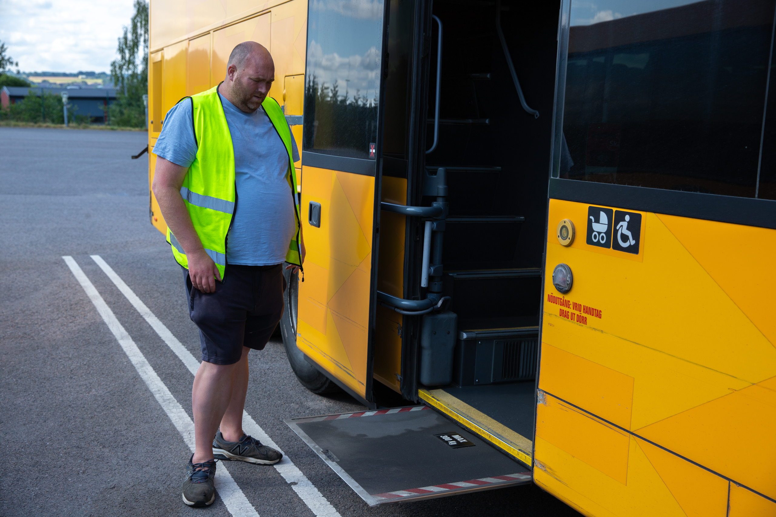 Man i gul varselväst står vid utdragen handikappramp på bussens sida.