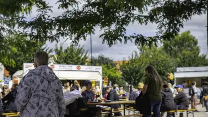 Serveringsområdet, folk sitter och äter vid långbord utomhus i solen
