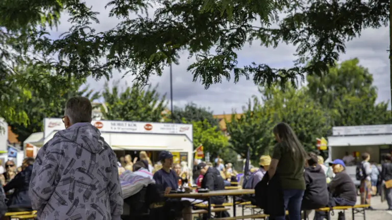 Serveringsområdet, folk sitter och äter vid långbord utomhus i solen