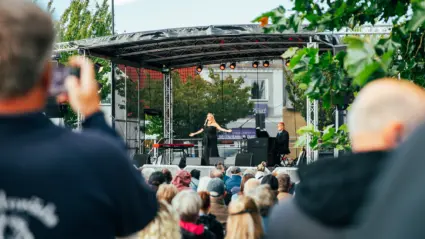 En kvinna i svart klänning sjunger framför en publik på en utomhusscen.