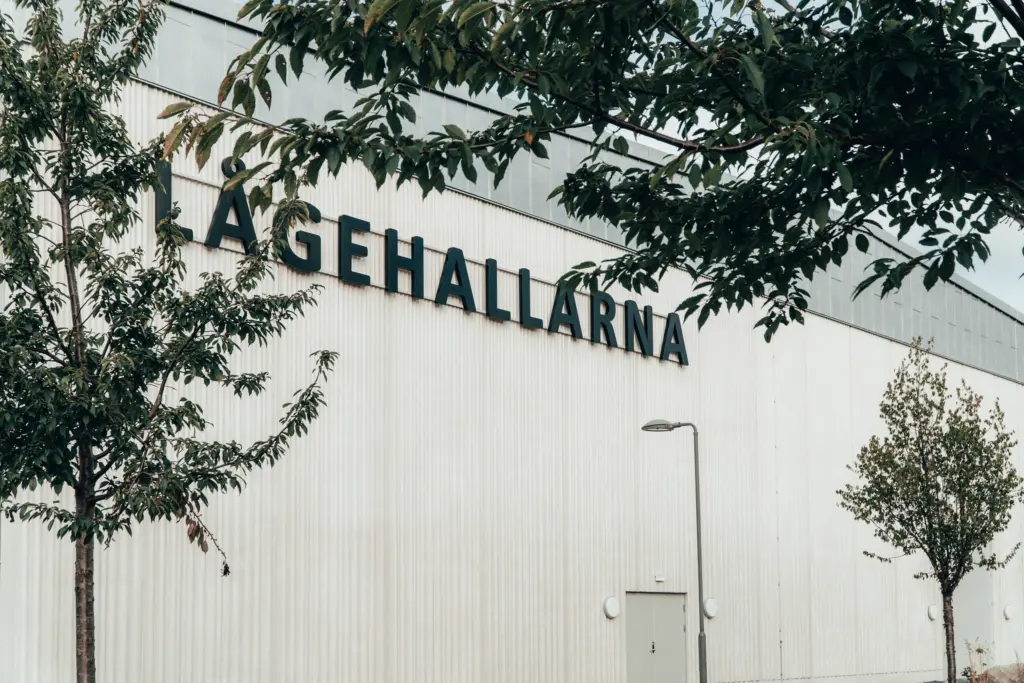 Namnet "Lågehallarna" på en byggnads ena sidan genom ett lövverk.