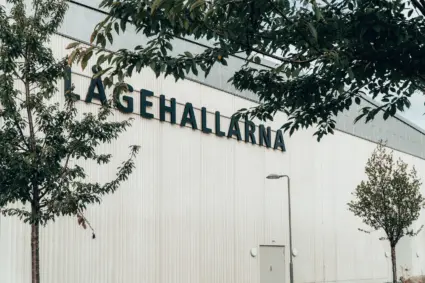 Namnet "Lågehallarna" på en byggnads ena sidan genom ett lövverk.