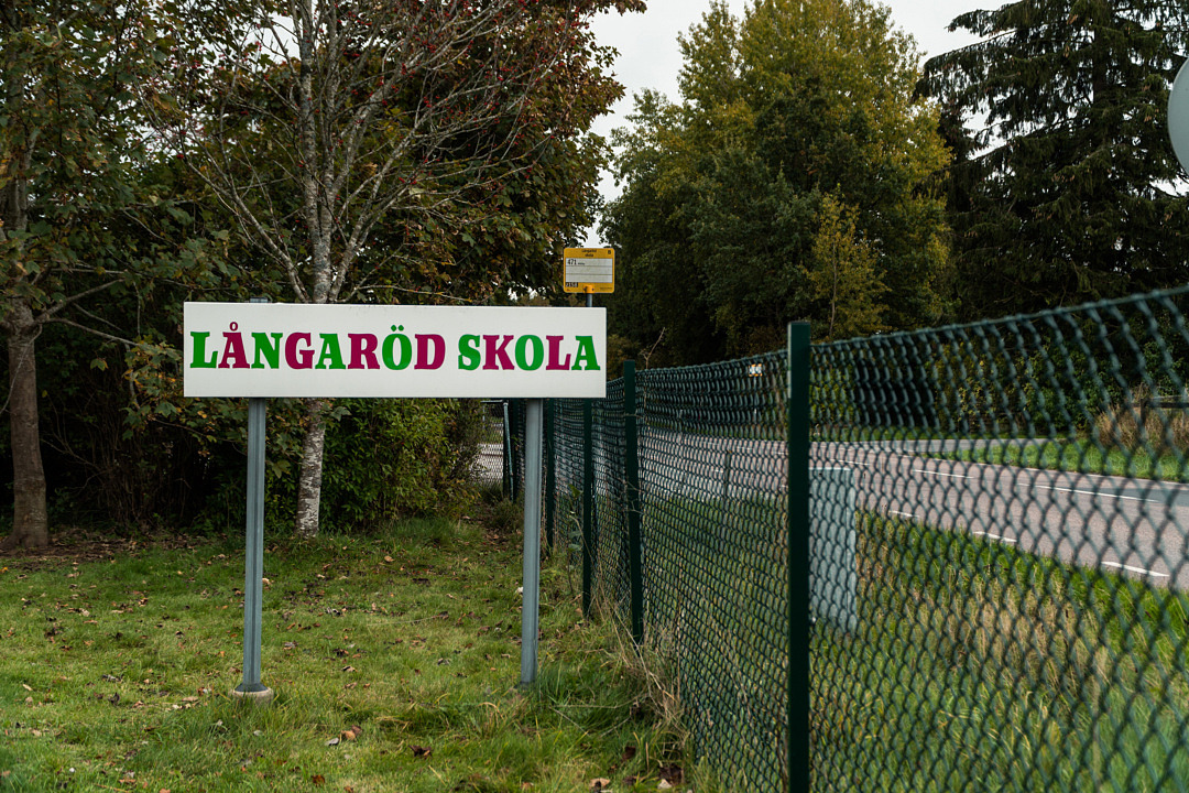 En skylt intill ett staket och en väg med texten: Långaröds skola.