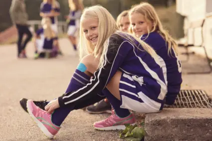 Porträtt av glad tjej som knyter skosnören bredvid kompisar