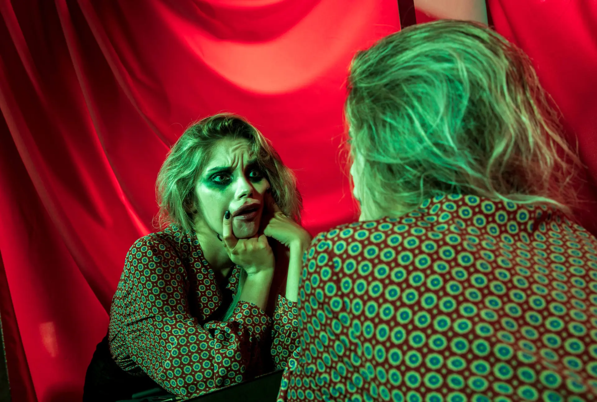 Teatersminkad ung kvinna gör grimas mot sig själv i spegeln