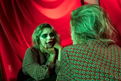Teatersminkad ung kvinna gör grimas mot sig själv i spegeln