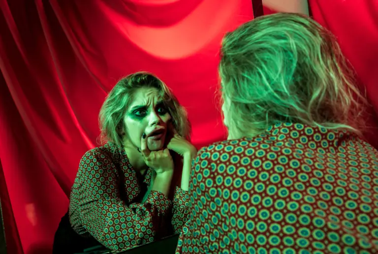 Teatersminkad ung kvinna gör grimas mot sig själv i spegeln