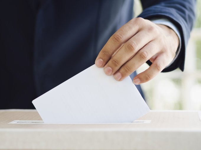 Närbild på hand som lägger ett vitt kuvert i en låda.