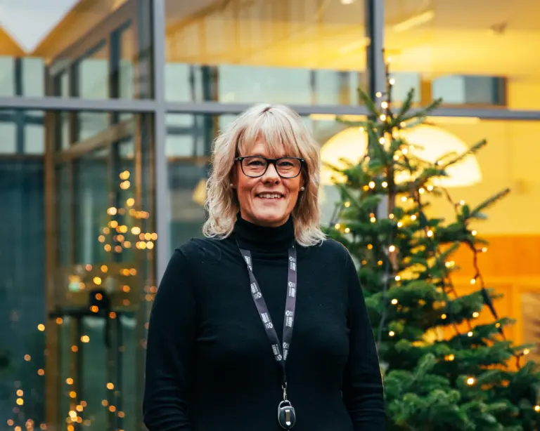 Kvinna i glasögon står framför pyntad julgran.