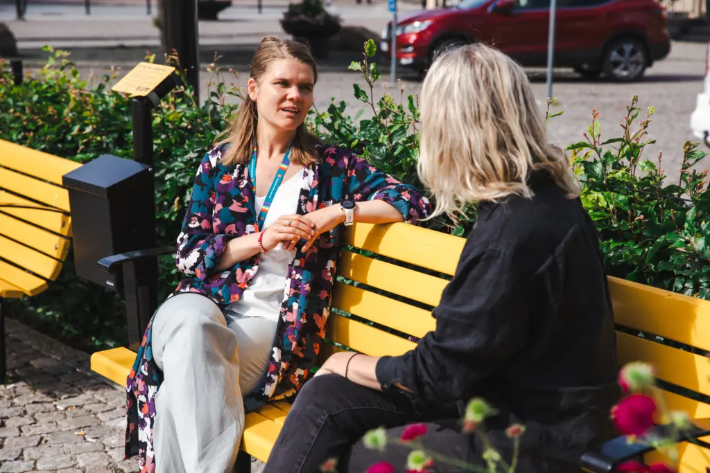 två kvinnor sitter på gul bänk