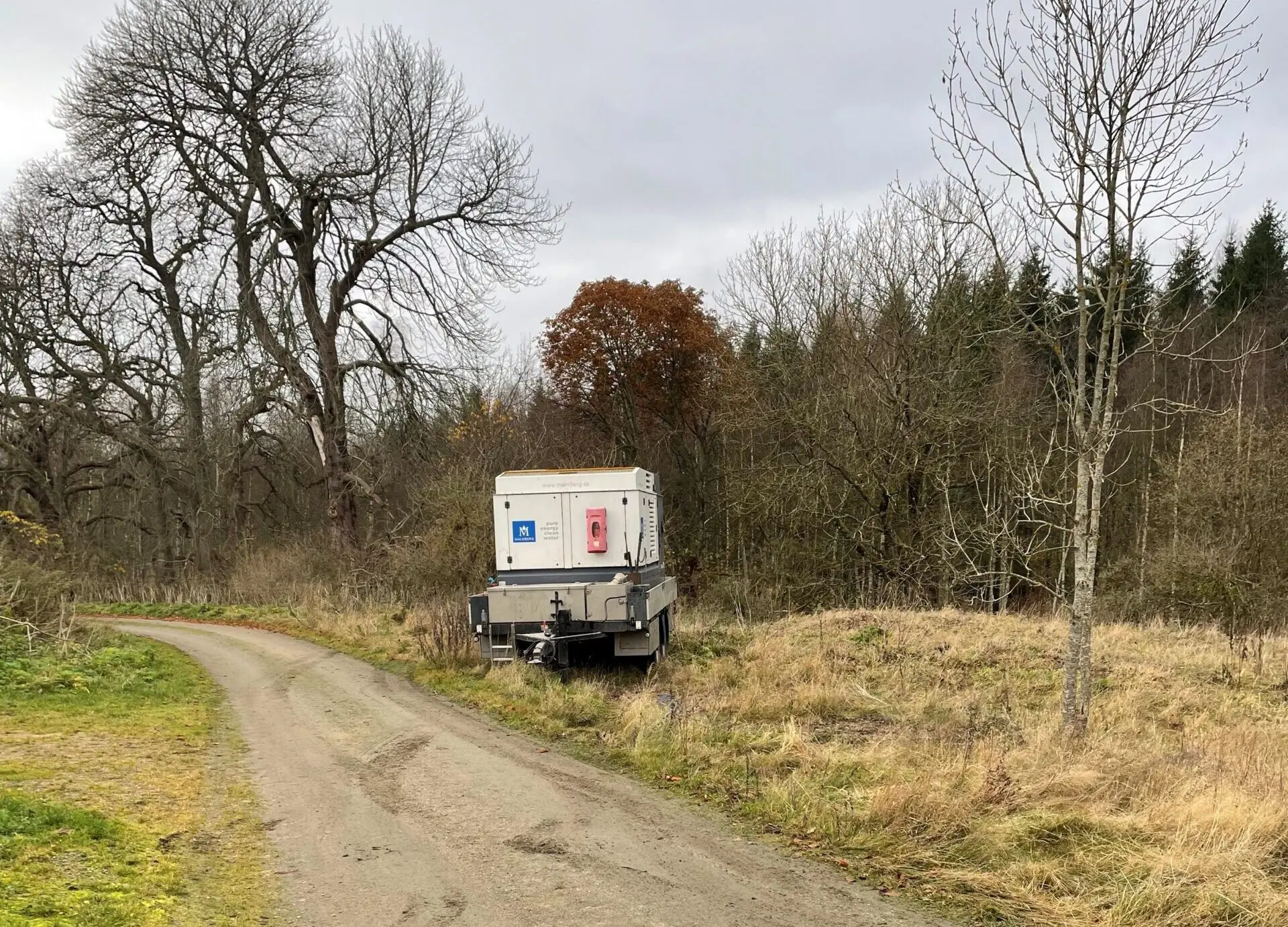 Grusväg i ett skogsbryn med en vagn stående i vägkanten