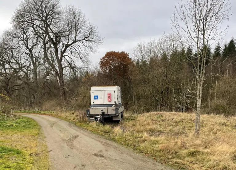 Grusväg i ett skogsbryn med en vagn stående i vägkanten