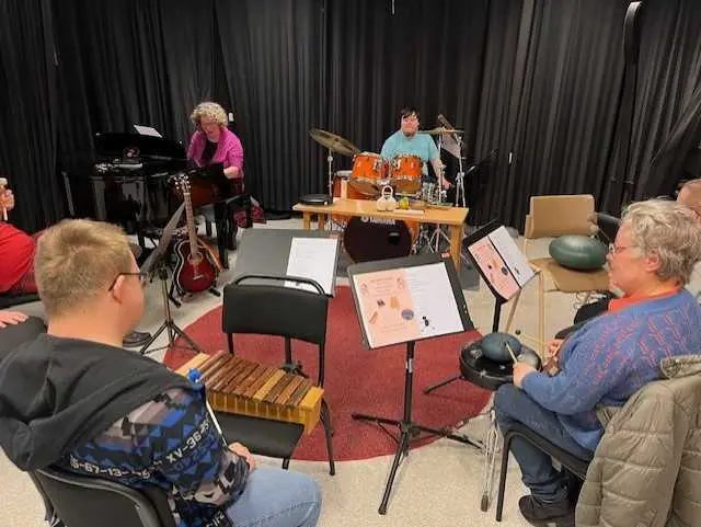 Personer sitter i en cirkel med notst&auml;ll och instrument som xylofon och slagverk mellan sig.