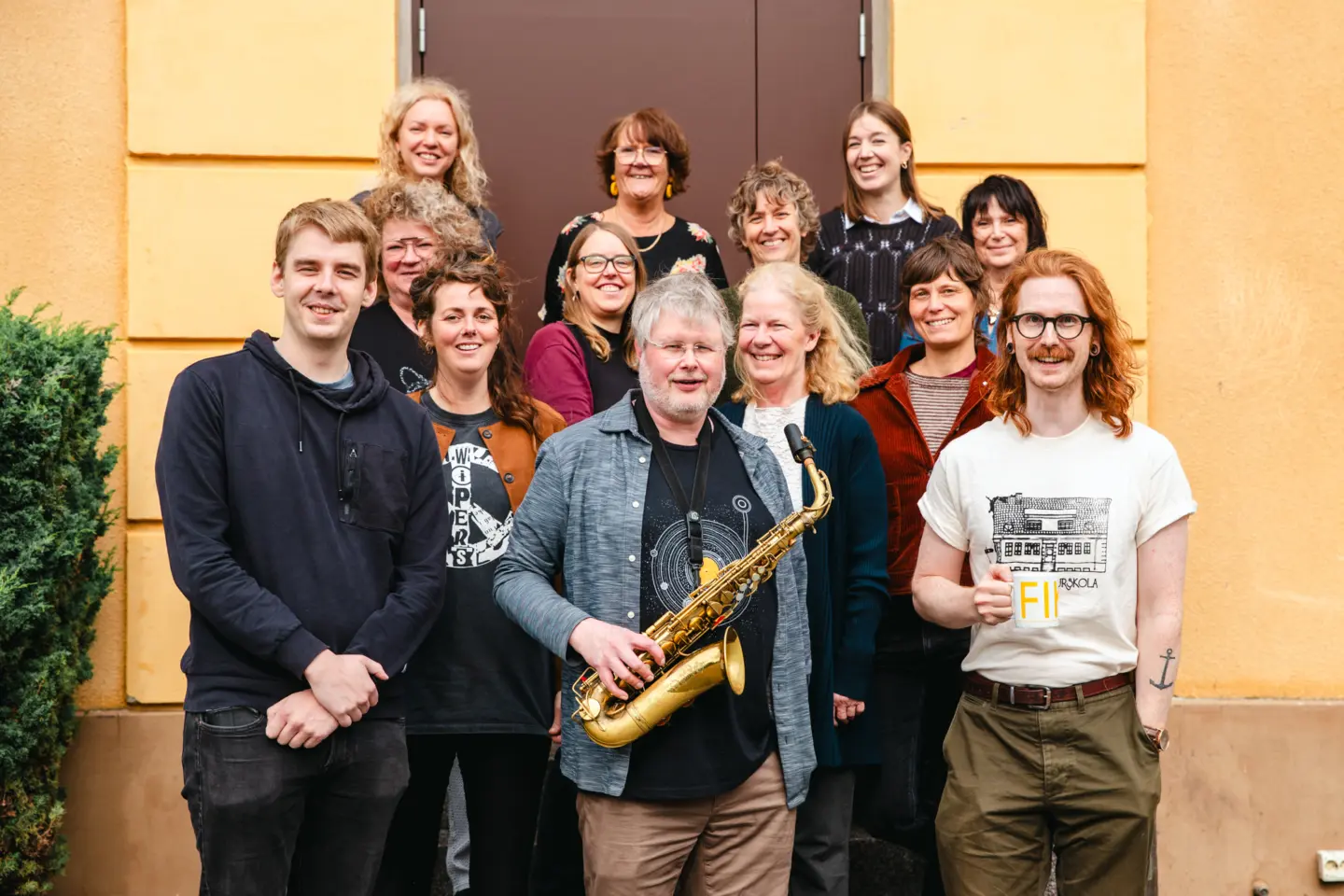 En grupp människor står utomhus framför en gul fasad. De ler mot kameran.