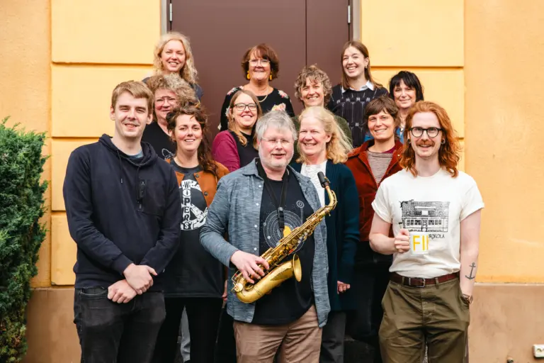 En grupp människor står utomhus framför en gul fasad. De ler mot kameran.