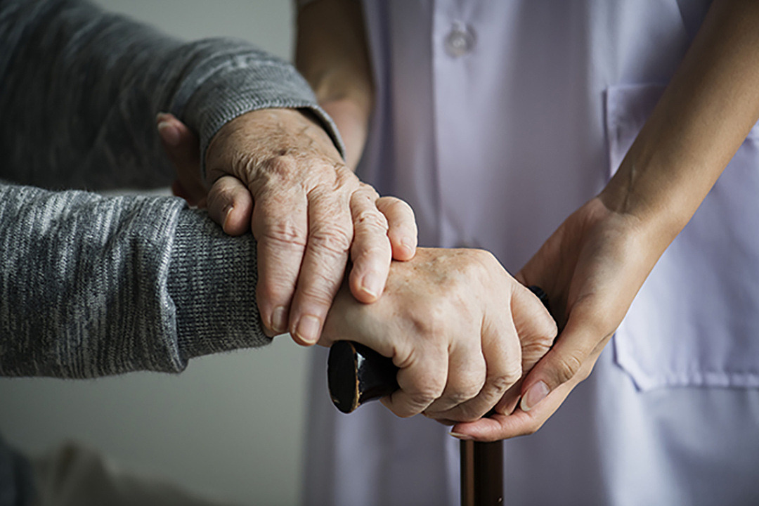 Närbild på händer som stöttar en äldre person.