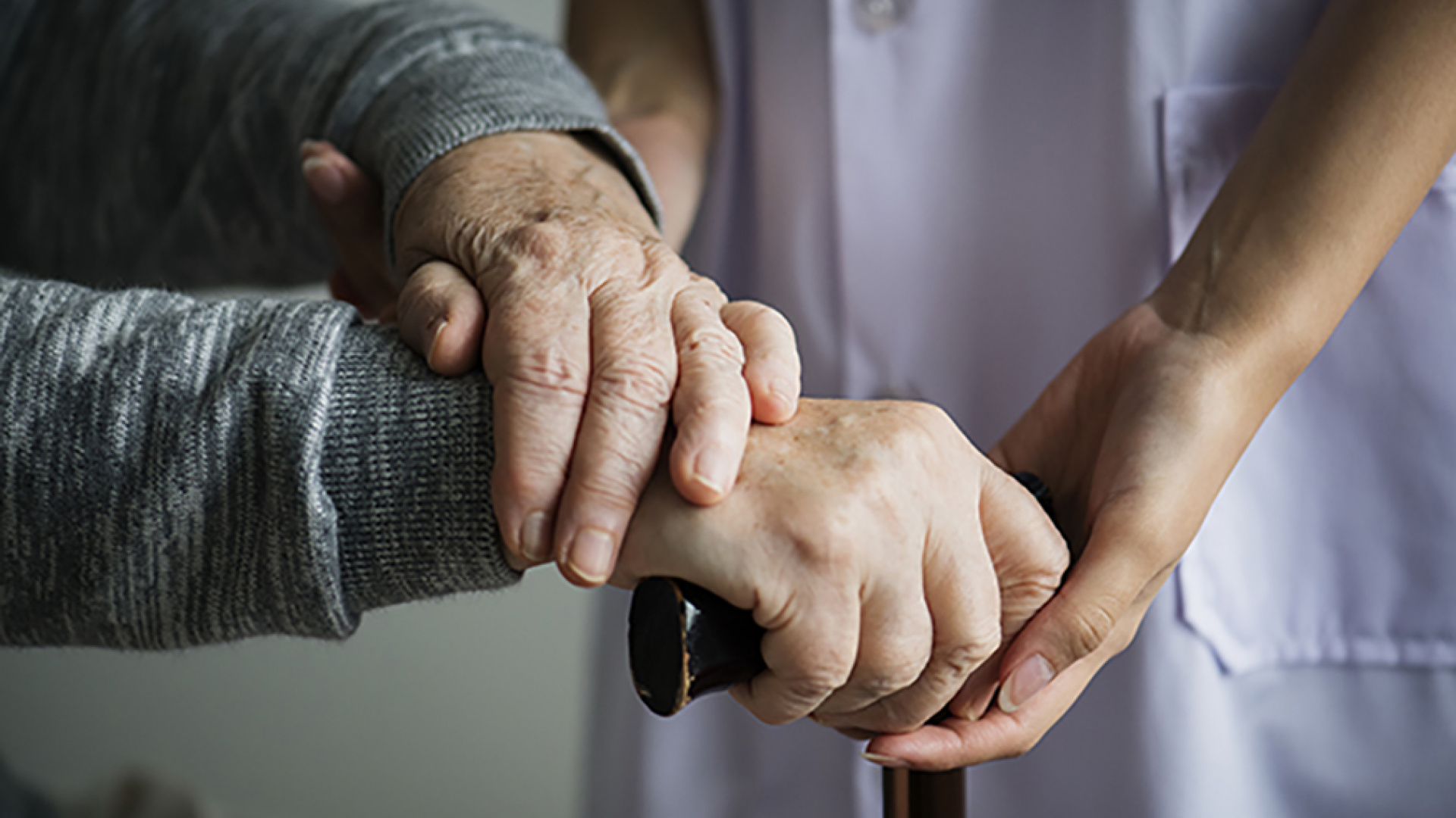 Närbild på händer som stöttar en äldre person.