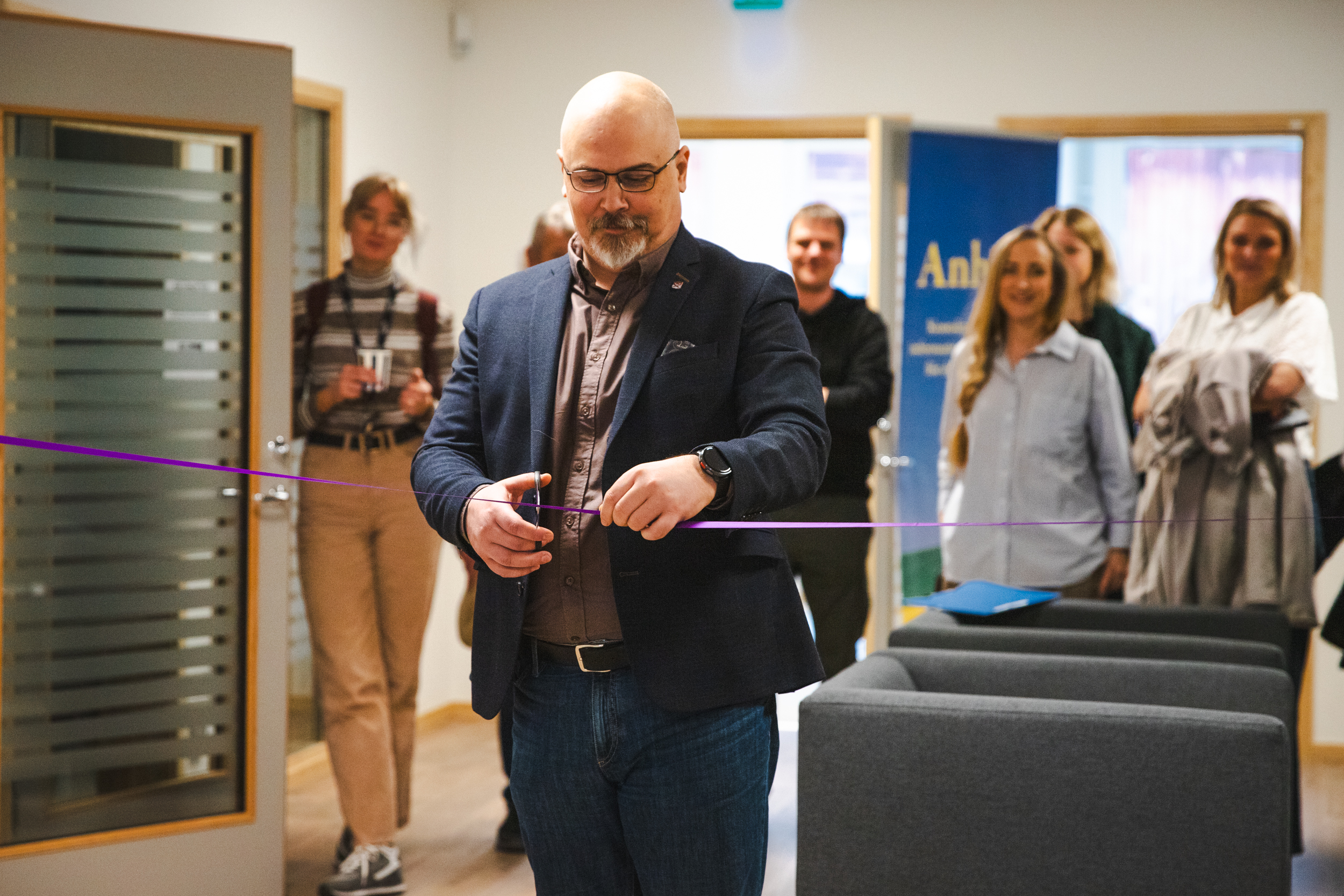 En man klipper av ett lila invigningsband. Glada åskådare står i bakgrunden.