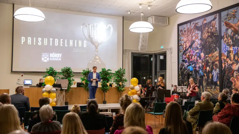 Människor i en stor lokal är publik där en man agerar som konferencier.