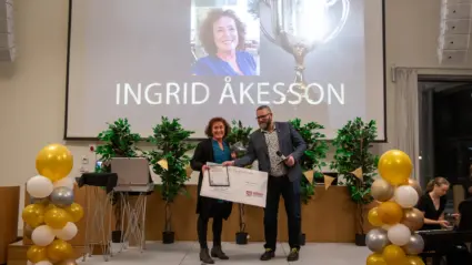 Kvinna står på ett podie och får motta en utmärkelse av en man.