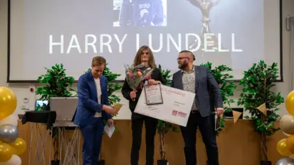 Ung man står på ett podie där han får ta emot en utmärkelse av två män.