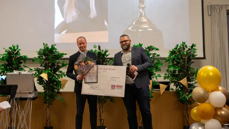 Två män står på ett podie där den ena får motta en utmärkelse.