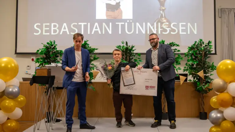 Ung man står tillsammans med två män på ett podie och får motta en utmärkelse.