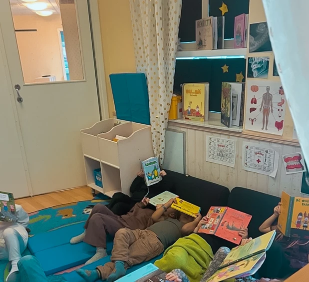 Ett gäng barn ligger på golvet på kuddar och filtar med böcker uppslagna framför ansiktet.