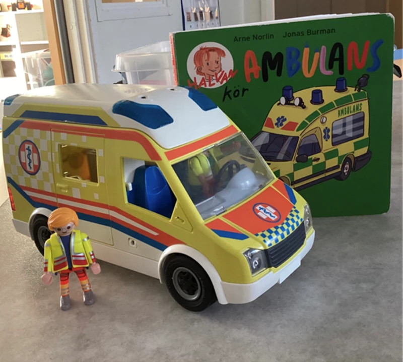 En bok om en ambulans st&aring;r uppst&auml;lld bredvid en leksaksambulans och en figur av en man.