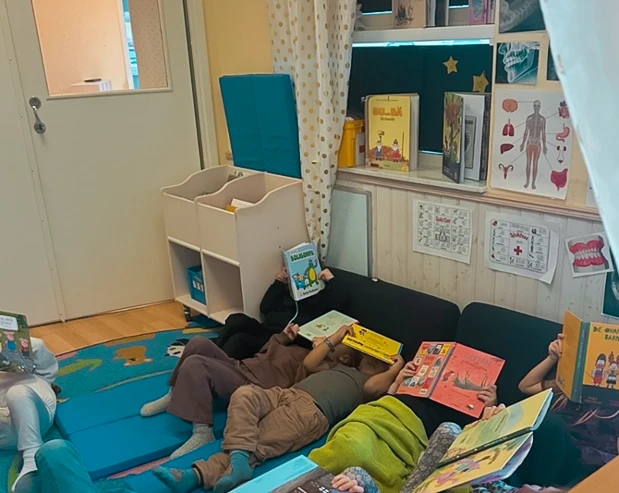 Ett gäng barn ligger på golvet på kuddar och filtar med böcker uppslagna framför ansiktet.