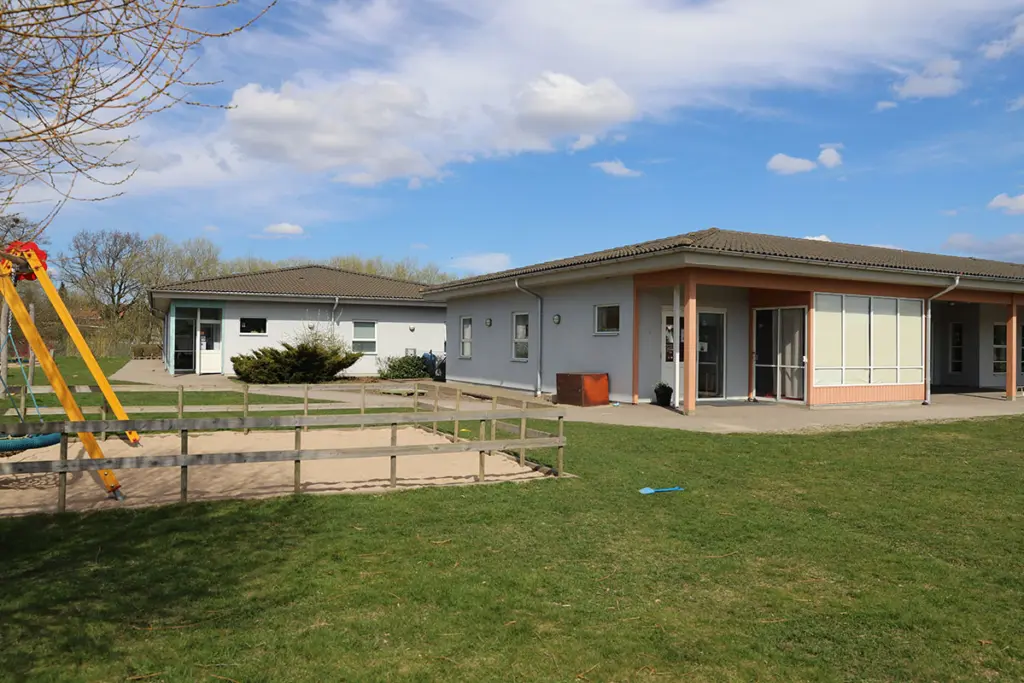 Förskolebyggnad med grönområde utanför och en gunga.