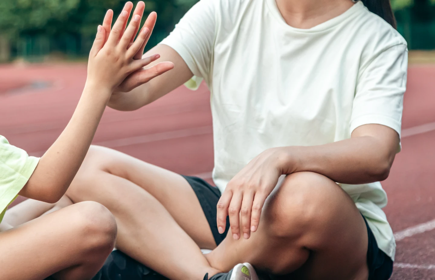 vuxen idrottsledare gör high five med ett barn, sittande på en löpbana