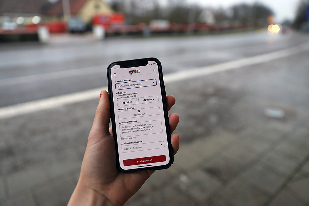 Hand håller en smartphone med appen Tipsa Hörby på skärmen.