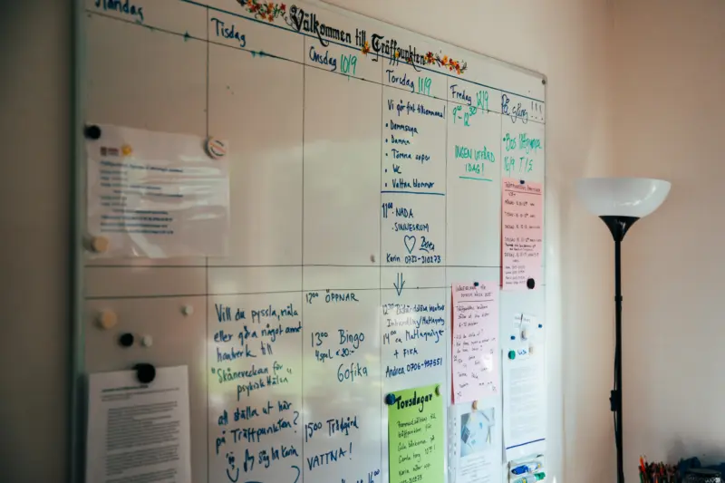 En bild på en väggfast whiteboardtavla med många färgglada lappar med information samt ett stort veckoschema med veckans aktiviteter