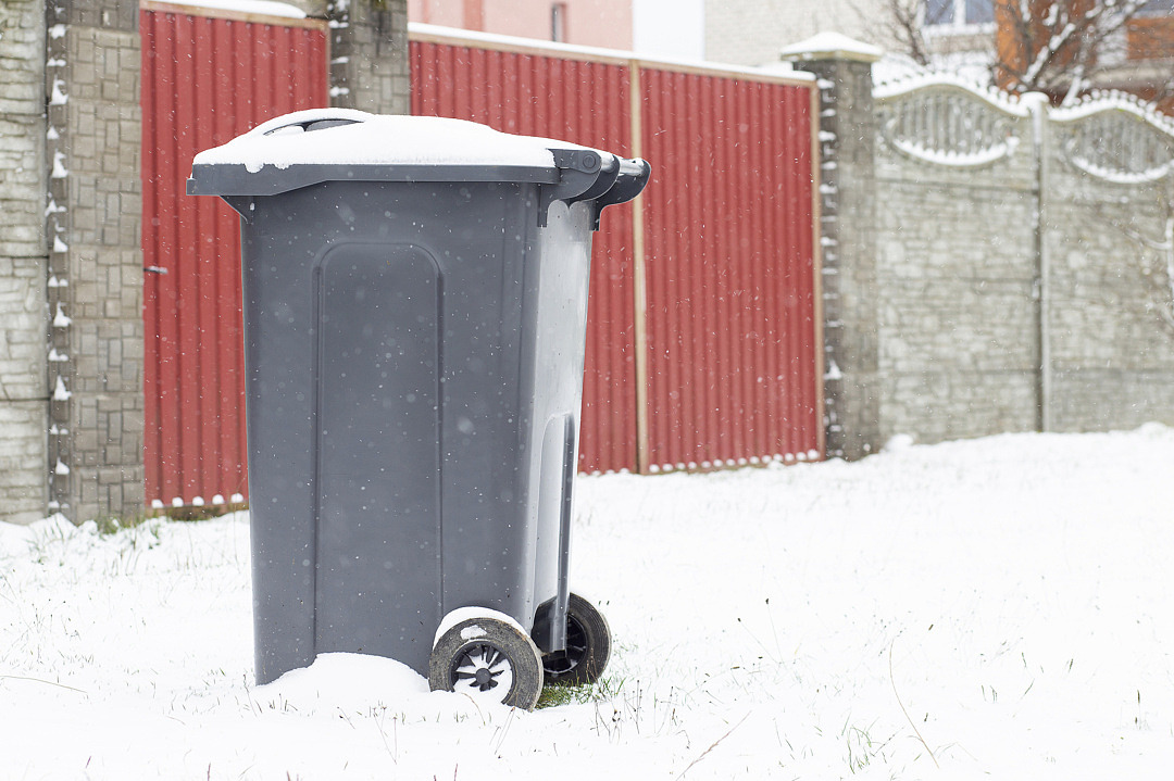 Soptunna framför grind på snötäckt mark.