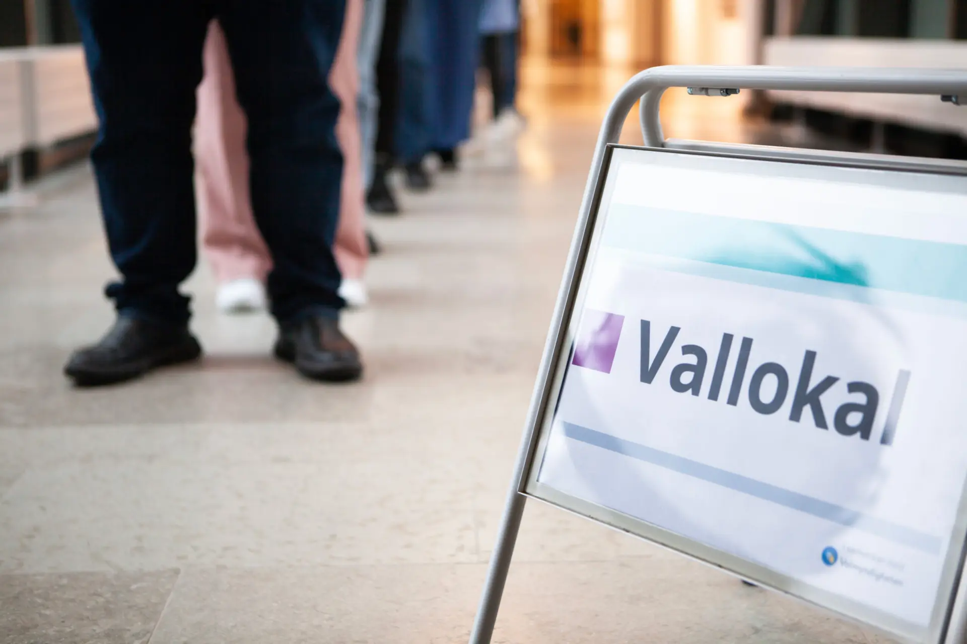 Skylt med ordet "Vallokal" bredvid en kö av människor.