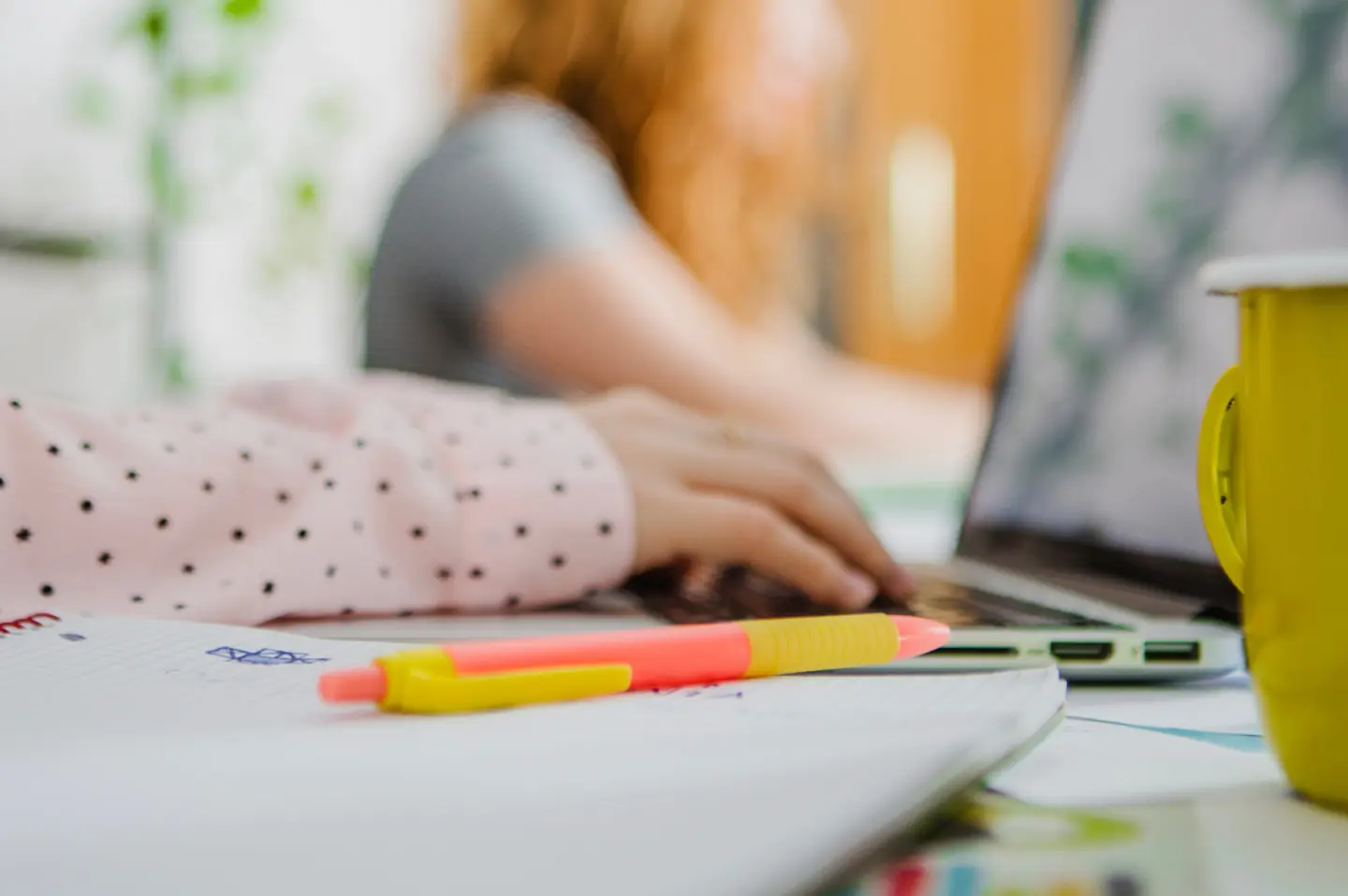 Närbild på flickas arm som skriver på en laptop, med penna och anteckningsblock i förgrunden